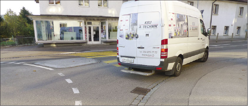 Les Breuleux (JU) - Grand'Rue, Lieferwagen ausgangs des Kreisverkehrs befährt Fussgängerbereich